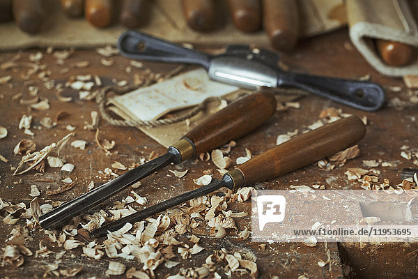 Nahaufnahme von Holzschnitzerei-Handwerkzeugen  Stemmeisen und Holzspänen auf einer Bank in der Werkstatt eines Schnitzers.