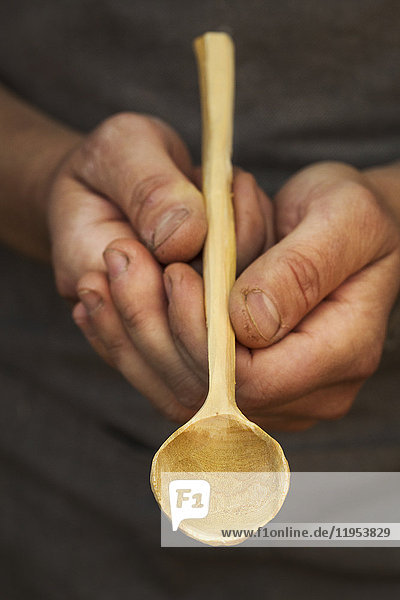Die Hände eines Mannes halten einen handgefertigten Holzlöffel mit langem schlanken Stiel und runder polierter Schale.