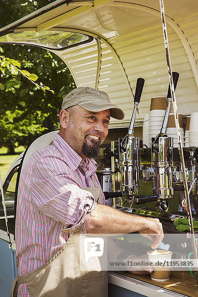 Bearded man wearing apron standing by blue mobile coffee shop  making coffee.