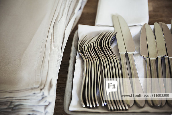 High angle close up of napkins and silver forks and knives on a table in a restaurant.
