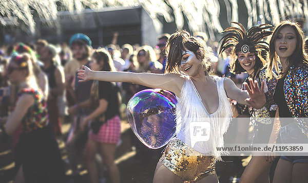 Junge Frau bei einem Sommer-Musikfestival,  die in goldenen,  mit Pailletten bestickten Hotpants unter der Menge tanzt.