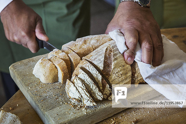 Nahaufnahme einer Person  die einen frisch gebackenen Brotlaib aufschneidet.