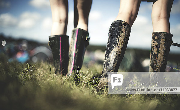 Rückansicht mit niedrigem Querschnitt von zwei jungen Frauen bei einem Sommer-Musikfestival  die schlammige Wellington-Stiefel tragen.