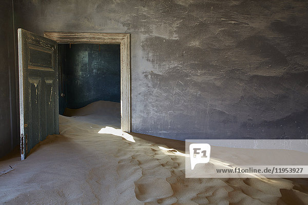Ein verlassenes Gebäude  eine offene Tür und Sandverwehungen  die vom Rest des Gebäudes in den Raum eindringen. Eine Geisterstadt.