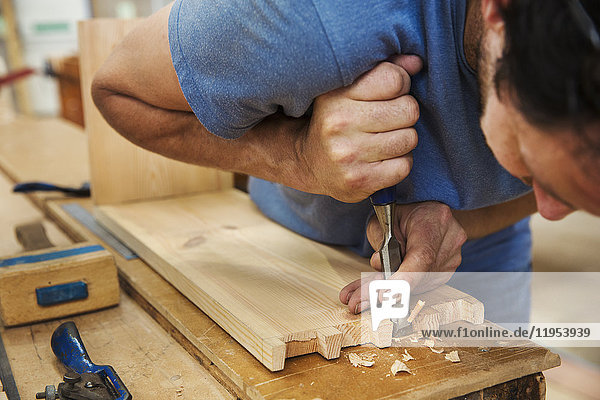 Nahaufnahme eines Mannes  der in der Werkstatt eines Bootsbauers arbeitet und zwei Holzstücke zusammenfügt.