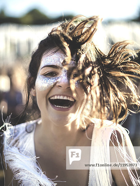Junge Frau mit langen braunen Haaren bei einem Sommer-Musikfestival mit geschminktem Gesicht  in die Kamera lächelnd.