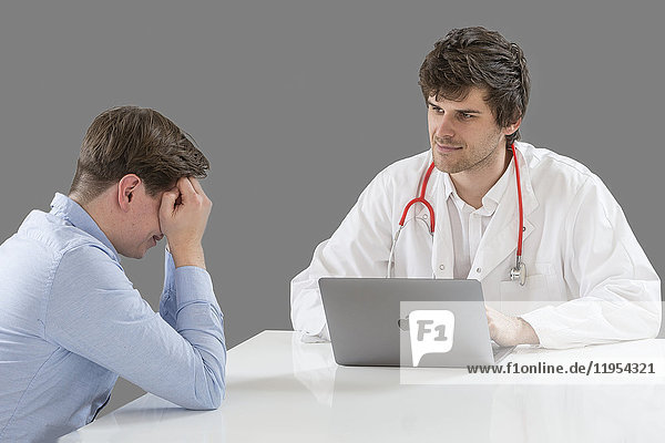 Arzt im Gespräch mit einem depressiven männlichen Patienten im Büro