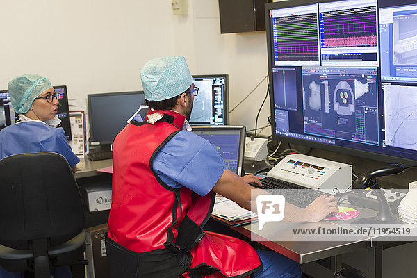 Reportage in der Abteilung für interventionelle Kardiologie und Rythmologie in der Klinik Saint George in Nizza  Frankreich. Radiofrequenzablation von Herzrhythmusstörungen mit dem Robotersystem Stereotaxis. Bei diesem Eingriff wird ein Katheter in das Herz eingeführt  der Radiowellen aussendet  die das für die Rhythmusstörungen verantwortliche Herzgewebe veröden. Das Stereotaxis-Robotersystem ist ein magnetisches Navigationssystem. Es nutzt ein rotierendes Magnetfeld  das die Führung des Ablationskatheters aus der Ferne ermöglicht. Das System besteht aus zwei riesigen Magneten  die auf beiden Seiten des Operationstisches angebracht sind. Die Operation wird unter radioskopischer Kontrolle durchgeführt. Es handelt sich um eine präzisere Technik  die das Risiko von Komplikationen  die Dauer des Eingriffs und die Belastung des Patienten und des Radiologen durch Röntgenstrahlen verringert. Behandlung eines Patienten  der unter linkem Vorhofflattern leidet. Ein Techniker richtet das System ein und führt Tests durch.