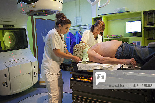 Reportage in der Strahlentherapieabteilung eines Krankenhauses in Savoie  Frankreich. Zwei Techniker bereiten einen Patienten für eine Strahlentherapie zur Behandlung eines zervikalen und dorsalen Adenokarzinoms vor. Eine Maske wird über den Patienten gestülpt  um seine Bewegungen während der Behandlung zu begrenzen.