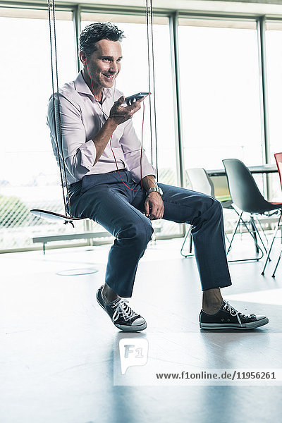 Geschäftsmann im Büro sitzend auf Schaukel  mit Smartphone