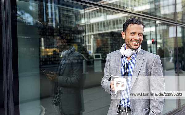 Smiling businessman with headphones and cell phone in the city