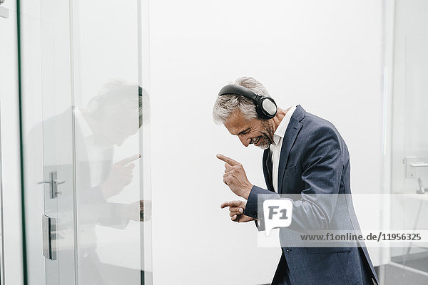 Happy mature businessman in office wearing headphones