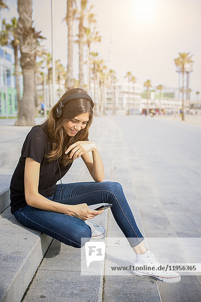 Smiling young woman sitting on steps listening to music