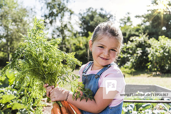 Porträt des lächelnden Mädchens im Garten mit Karottenstrauß