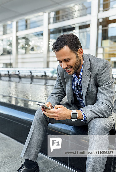 Smiling businessman sending messages with his smartphone in the city