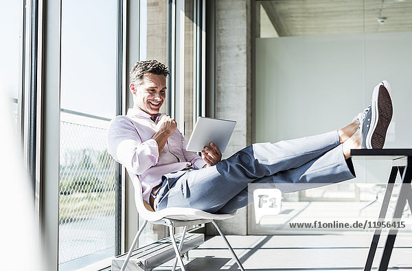 Geschäftsmann am Schreibtisch sitzend mit erhobenen Füßen  mit digitalem Tablett