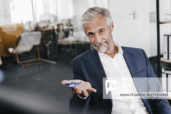 Portrait of mature businessman in office with fidget spinner