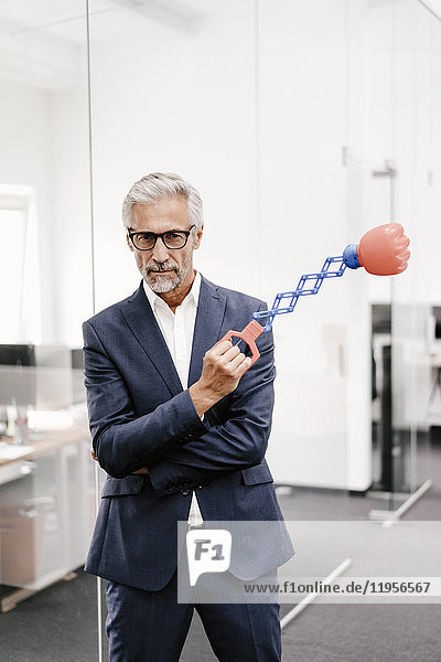 Mature businessman in office holding boxing toy