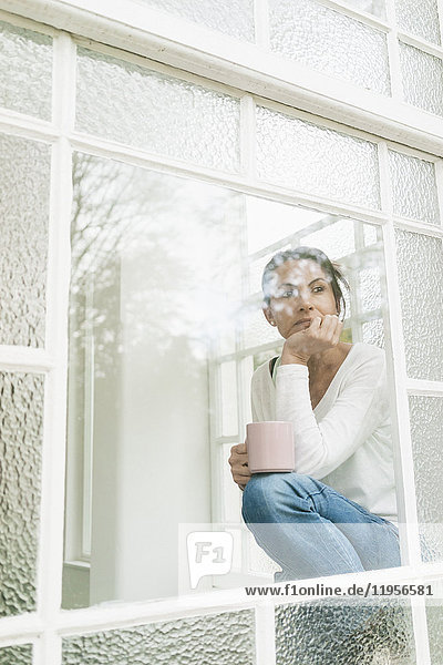 Nachdenkliche Frau mit einer Tasse Kaffee  die aus dem Fenster schaut.