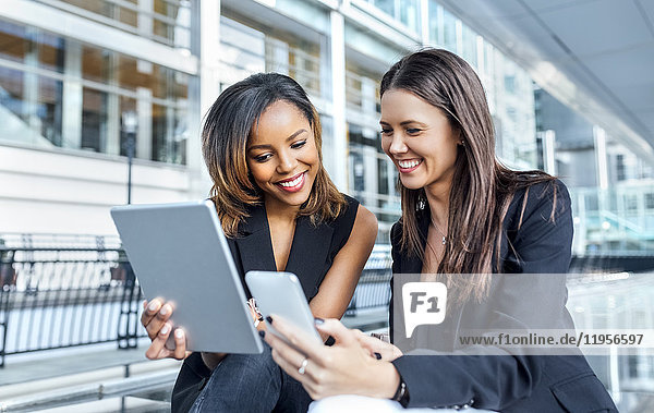 Two businesswomen working with smartphone and tablet in the city