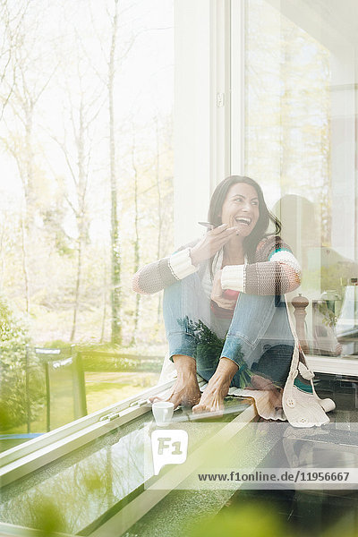 Laughing woman at home sitting on windowsill