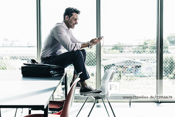 Businessman in office sitting on desk  using smartphone