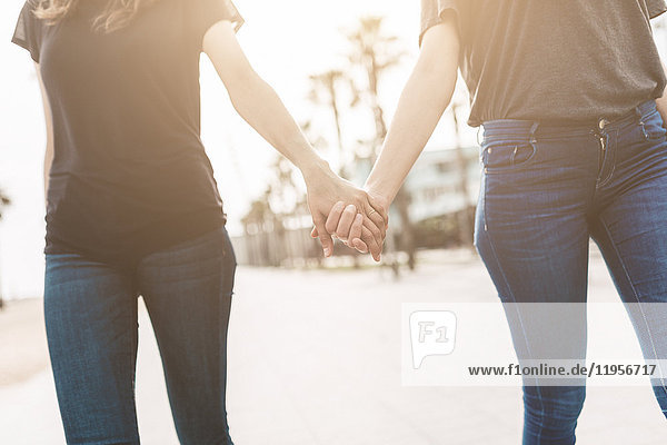 Zwei junge Frauen gehen Hand in Hand auf der Promenade.