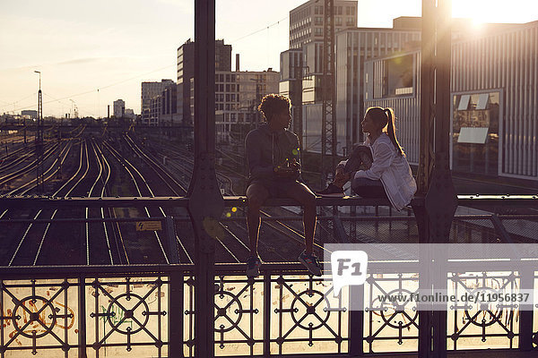 Germany  Munich  Young couple sitting on bridge  enjoying sunset