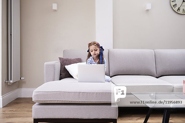 Little girl sitting on the couch looking at laptop