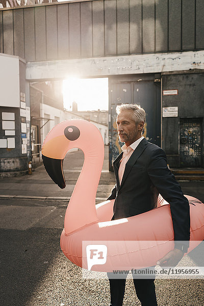 Erwachsener Geschäftsmann auf der Straße mit aufblasbarem Flamingo