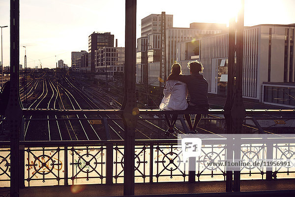 Deutschland  München  Junges Paar auf der Brücke sitzend  Sonnenuntergang genießend