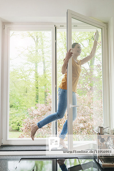 Glückliche Frau steht auf der Fensterbank und putzt das Fenster.