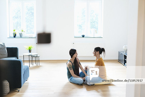 Two women sitting on wooden floor at home talking