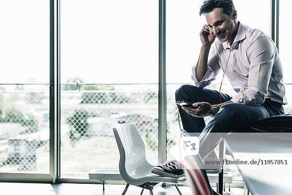 Geschäftsmann im Büro auf dem Schreibtisch sitzend  mit Smartphone