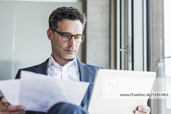 Portrait of serious businessman with documents looking at tablet