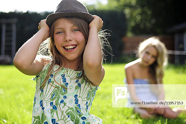 Happy playful girl putting on a hat in garden