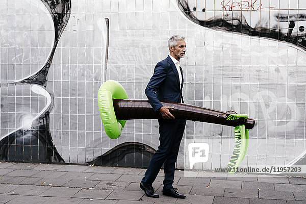 Mature businessman outdoors with inflatable palm tree