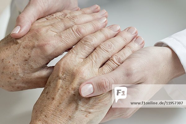 MODELL FREIGEGEBEN. Eine Ärztin untersucht die Hände eines älteren Patienten.