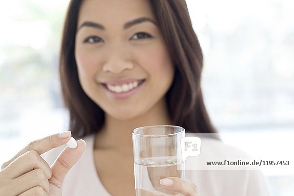 Young woman holding pill and glass of water.