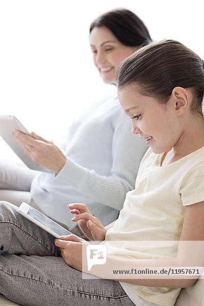 Mutter und Tochter auf dem Sofa mit digitalen Tablets.