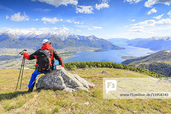 Hiker on green meadows admires Lake Como framed by snowy peaks  Montemezzo  Alpe Zocca  Lombardy  Italian Lakes  Italy  Europe