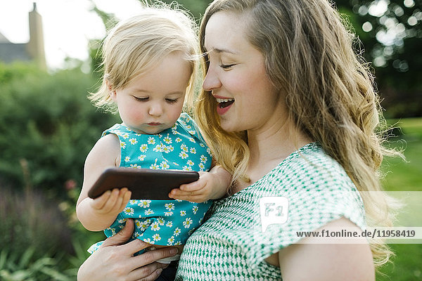 Mutter trägt Tochter (12-17 Monate)  Tochter spielt mit Smartphone