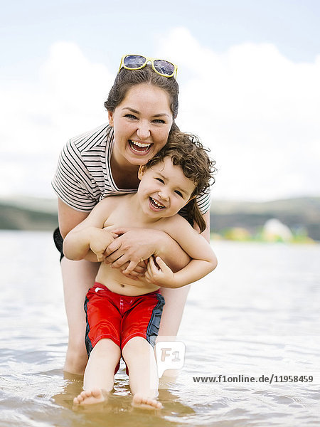 Porträt einer lachenden Mutter mit ihrem Sohn (4-5)  der im See watet