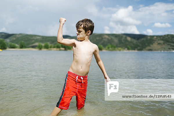 USA  Utah  Park City  Boy (6-7) flexing muscles while wading in lake