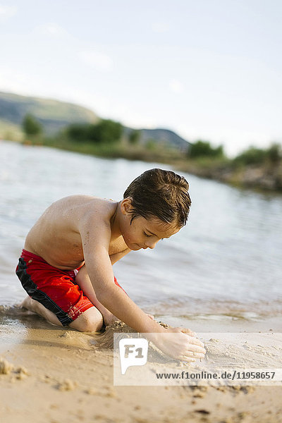Junge (6-7) spielt am Strand am See