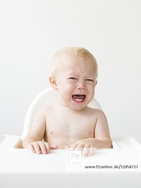Porträt eines kleinen Jungen (12-17 Monate)  der im Hochstuhl sitzt und weint