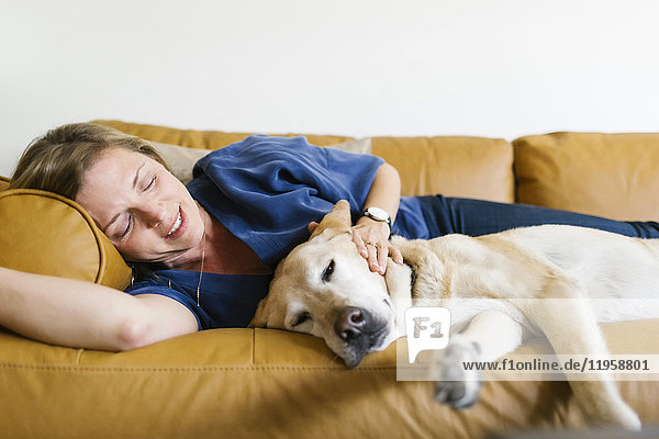 Frau und Labrador Retriever liegen auf dem Sofa