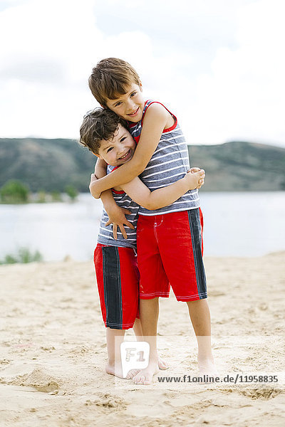 Brothers (4-5  6-7) embracing on beach by lake