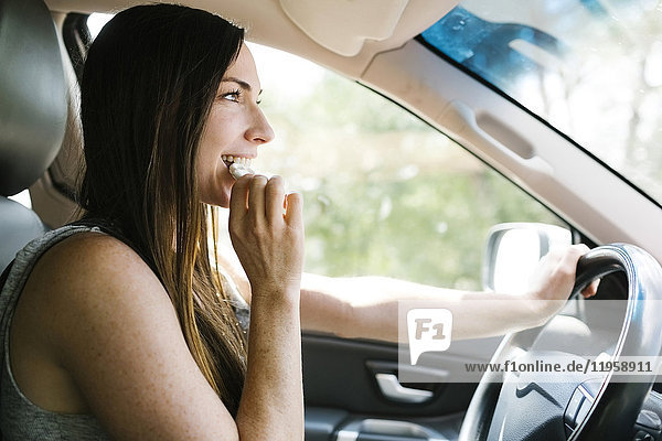 Lächelnde Frau fährt Auto und isst Brezel