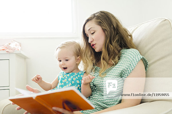Mother with baby girl (12-17 months) sitting in living room and reading book